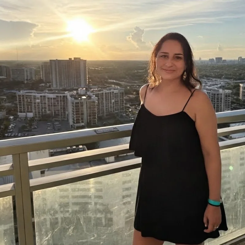 Maria Romo debout sur un balcon donnant sur une ville au coucher du soleil